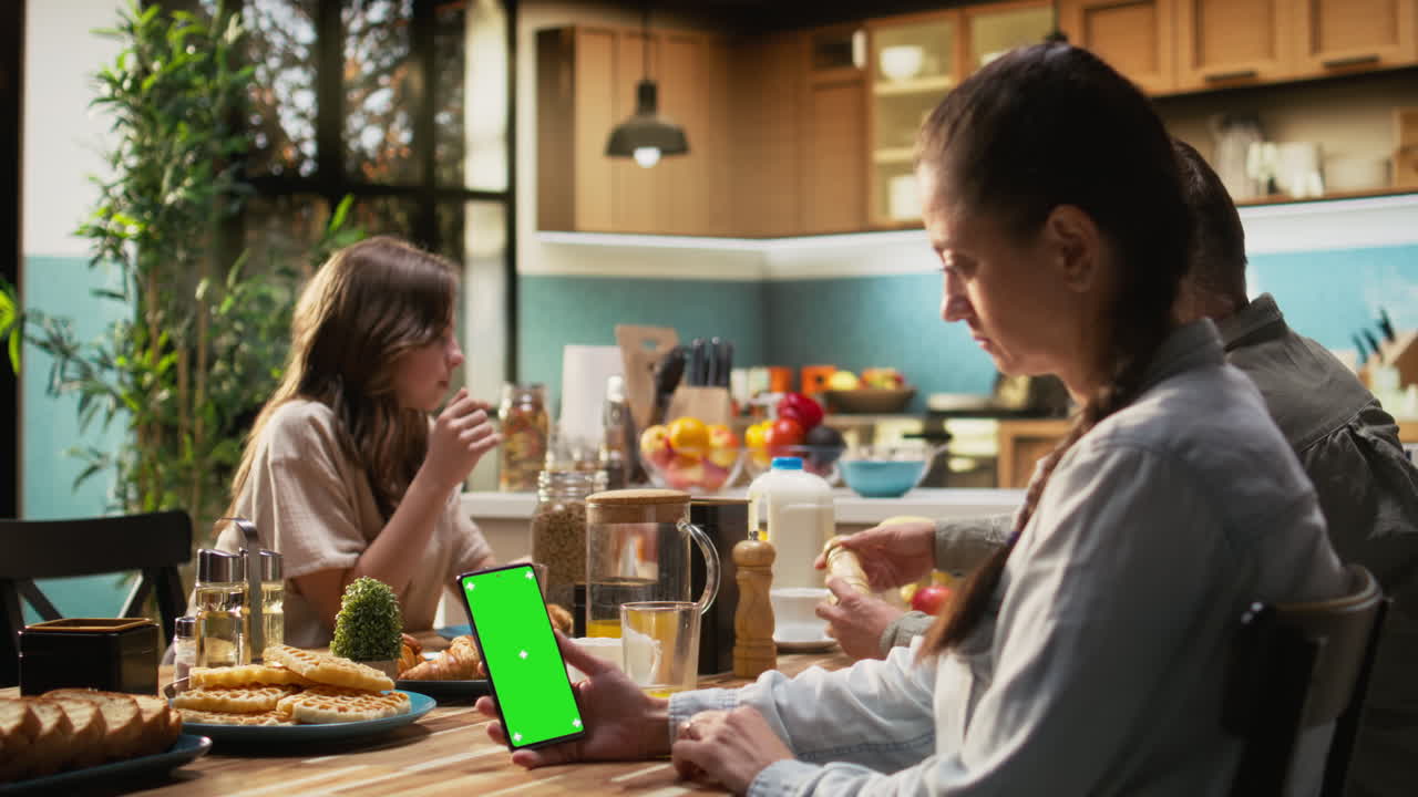 Vertical green screen smartphone held by mom serving breakfast with daughter