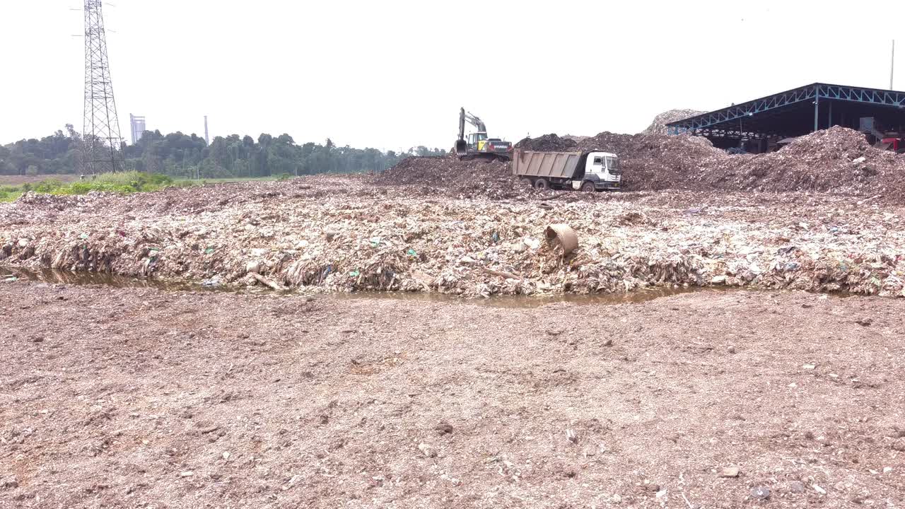 Close-up shot of a large, overflowing landfill or dump site with construction equipment managing piles of garbage and industrial waste