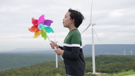 progressive young asian boy playing with wind turbine toy at wind turbine farm.