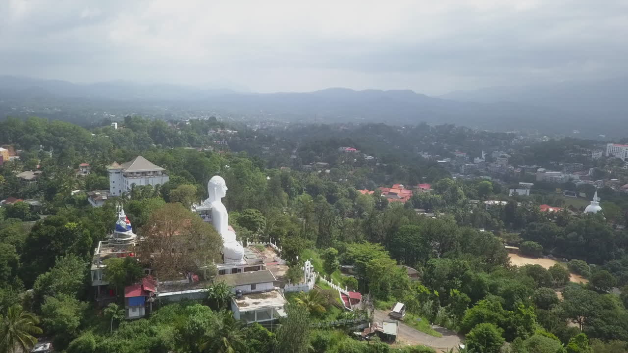 Aerial orbits Buddha statue in misty, hazy city of Kandy Sri Lanka