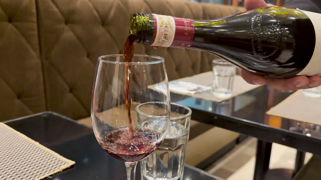 Un primer plano de vino tinto sirviéndose de una botella en una copa durante la cena