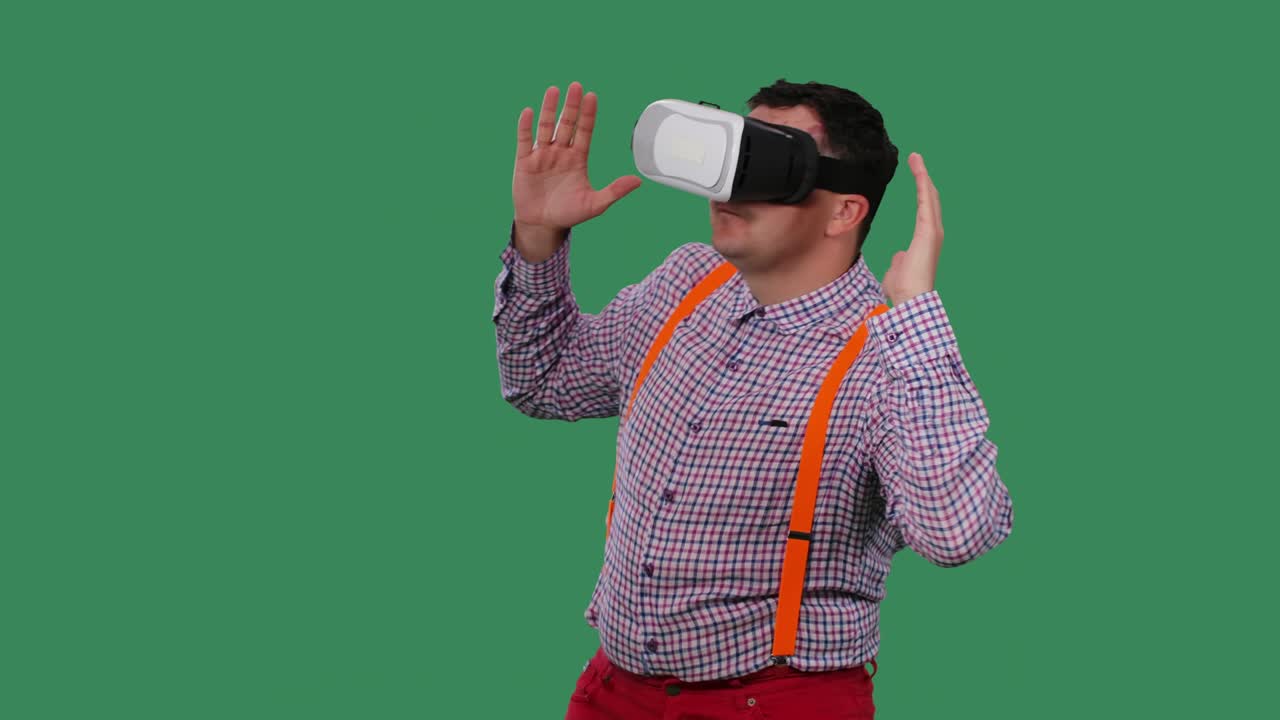 retrato de un hombre bailando con un auricular de realidad virtual o gafas 3d en la cabeza. un hombre con gafas, una camisa con tirantes naranjas en el estudio en una pantalla verde. cámara lenta. primer plano