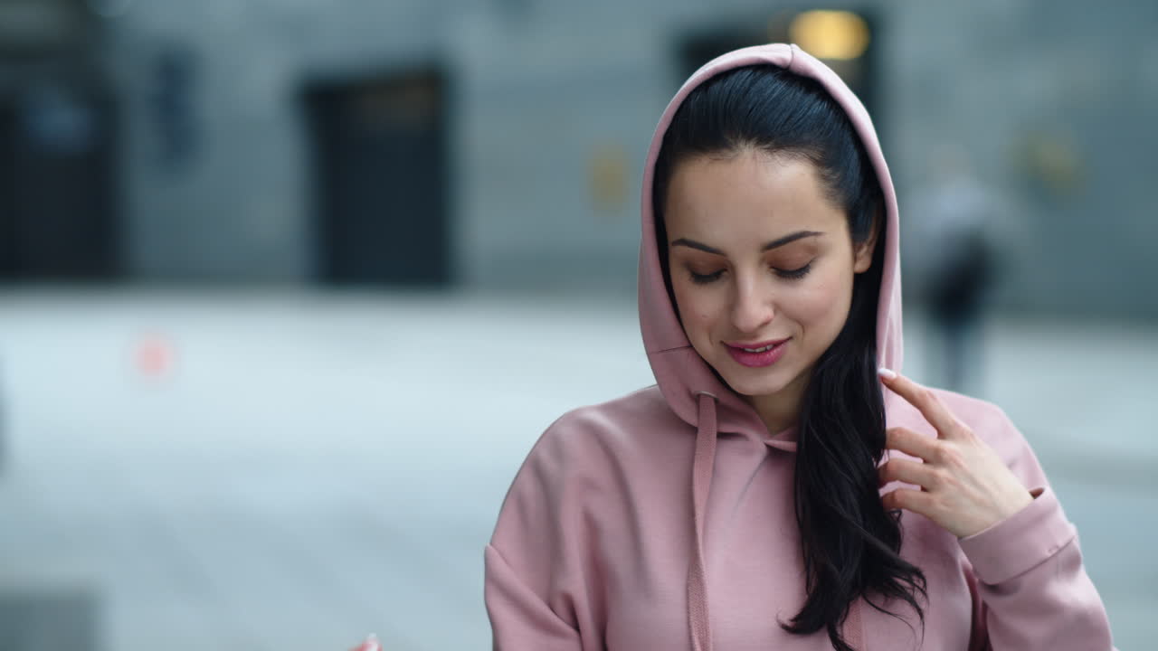 Fitnessfrau setzt draußen die Kapuze auf. Porträt einer lächelnden Frau im rosa Kapuzenpullover.
