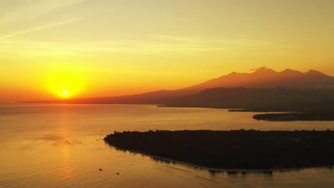 Yellow-sun-setting-down-mountain-island-horizon-reflecting-on-calm-sea-surface-around-silhouette-of-tropical-islands-in-Bali