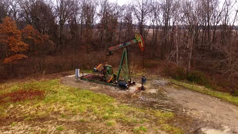 a fully working pump jack on the edge of a field with winter trees in the background