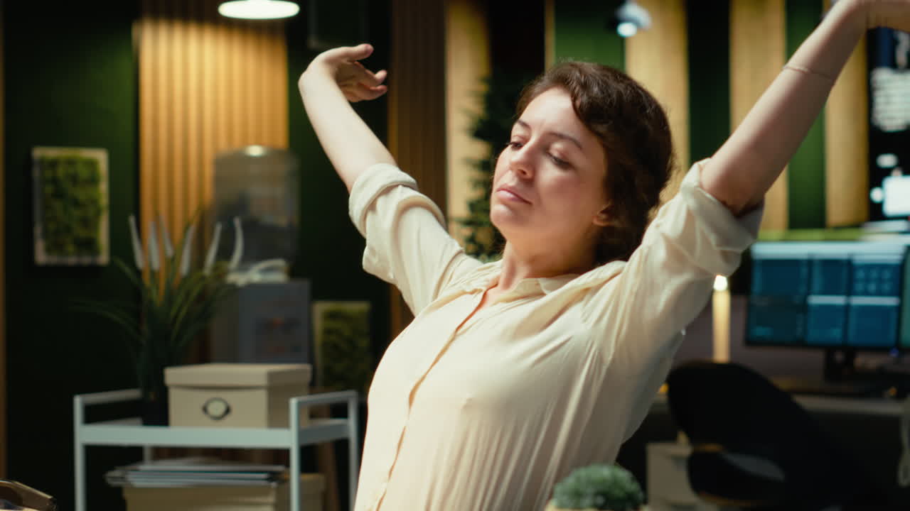 Vertical Video Woman in a dark office after hours leaning back in her office chair