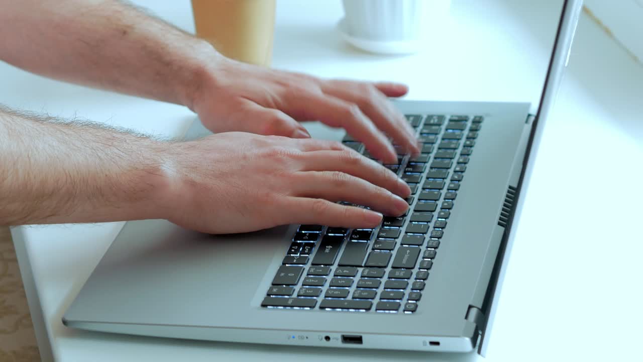 Male hands on the laptop keyboard typing, typing, office work, white desk