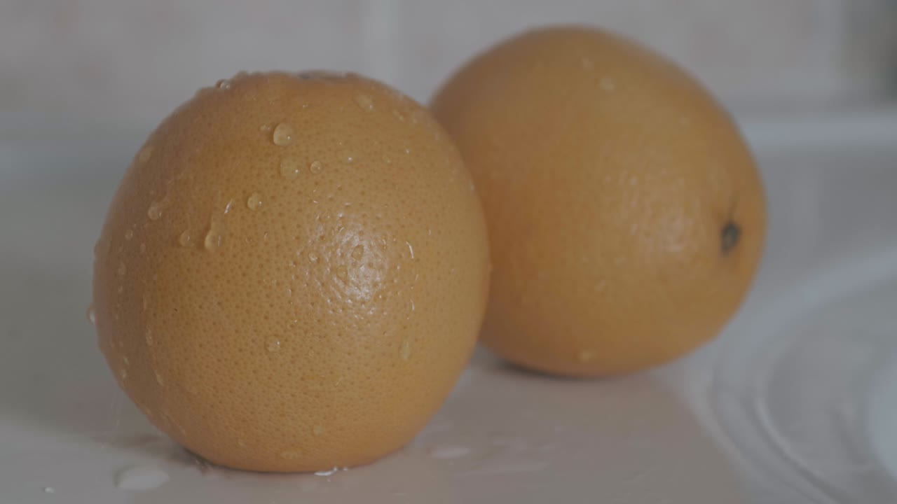 큰 오렌지 자몽에 물방울이 떨어지고 오른쪽에 또 다른 자몽이 배경에 있습니다.