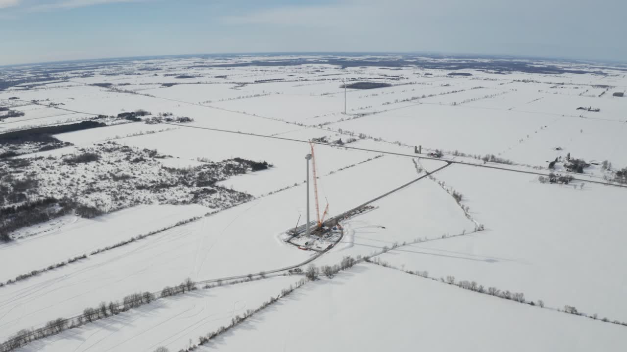 vista aérea de gran altitud desde un dron que se aleja del sitio de construcción de energía eólica en invierno con un paisaje cubierto de nieve
