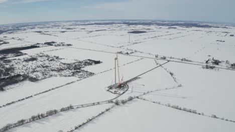 high altitude aerial view from drone backing away from wind energy construction site in winter with snow covered landscape