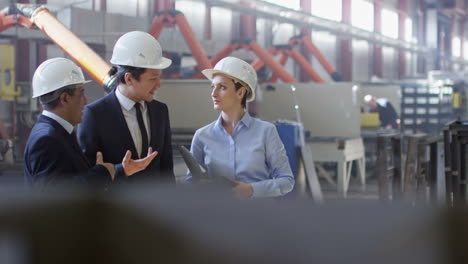 two businessmen and business woman dressed in smart clothes and helmets in a factory