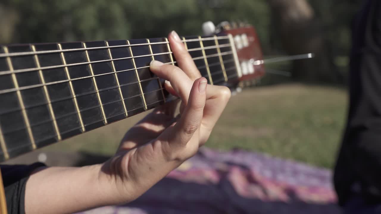 primer plano de una joven tocando la guitarra al aire libre, relajándose en el parque durante el día soleado