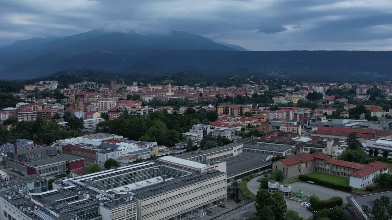 Group of buildings in Ivrea's Unesco-listed Olivetti district, framed by the Alps and Mount Mombarone in the background, drone shot, slow motion, sunny and cloudy sky, Piedmont, Italy