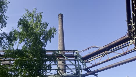 Gran-Chimenea-Vieja-Entre-árboles-Y-Viejas-Tuberías-De-Metal-Oxidado