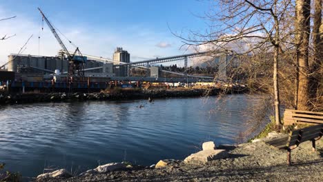 gran grúa azul en una barcaza amarrada en un muelle con al fondo un montón de transportadores de grano a un silo en un día parcialmente nublado