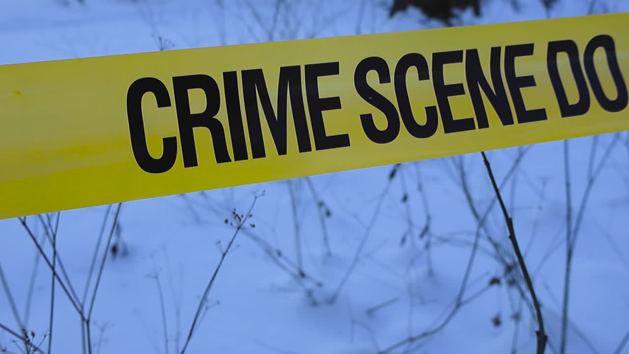 Close view of yellow crime scene police tape in snowy winter forest marking restricted forensic investigation area with shallow depth of field