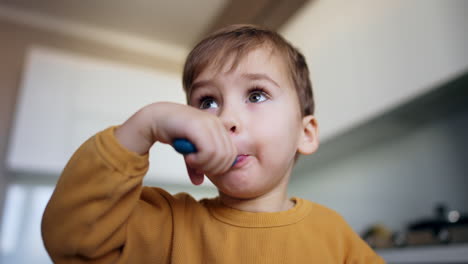 adorable baby boy takes a full spoon into his mouth. kid chews his food and waves his spoon in front of camera. low angle view.
