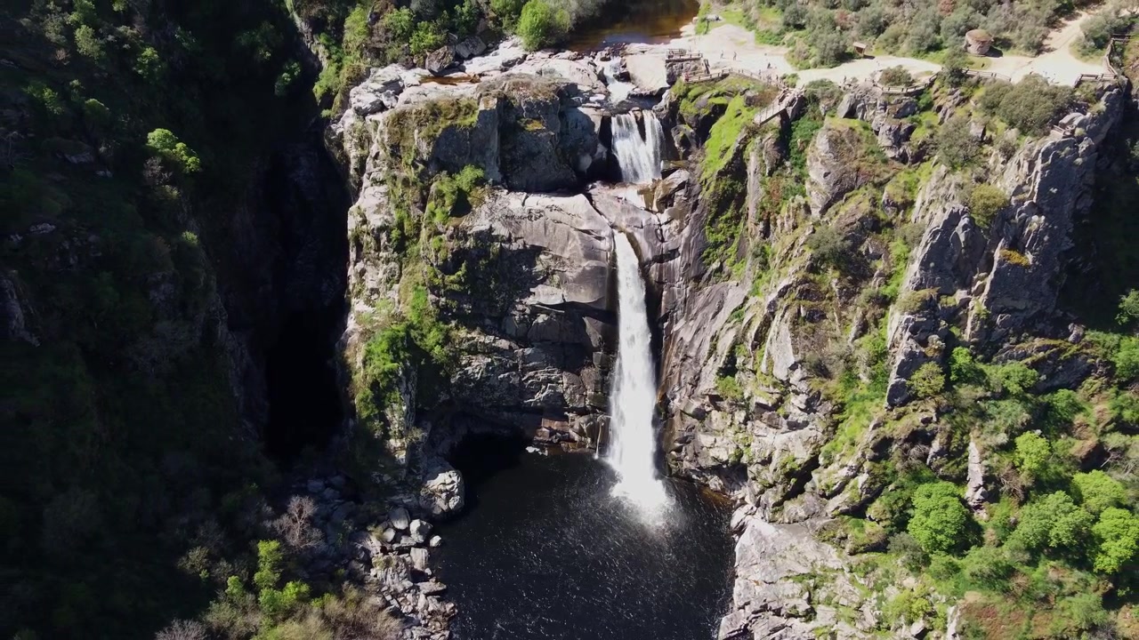 Ripresa aerea cinematografica 4K con drone che si avvicina lentamente alla spettacolare cascata Pozo de los Humos a Salamanca, Spagna. L'acqua ad alta pressione irrompe attraverso la scogliera rocciosa e si tuffa nella laguna scura