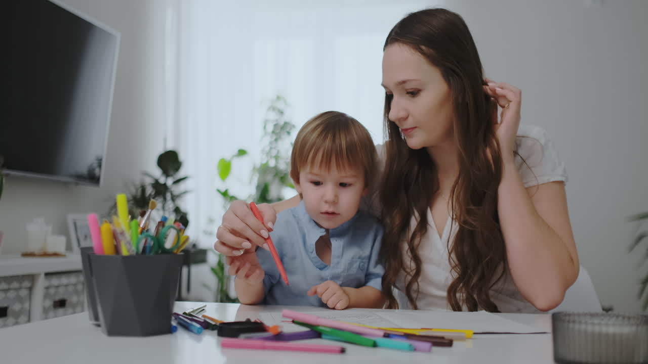 una familia de dos niños y una joven madre sentada en la mesa dibuja en papel con lápices de colores. desarrollo de la creatividad en los niños. interior blanco limpio