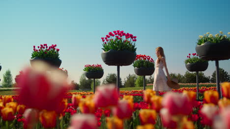 unknown woman in dress walking throught bright summer garden in blooming flowers