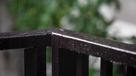 corner guardrail on a balcony with pouring rain splashing on the surface with a blurred garden background