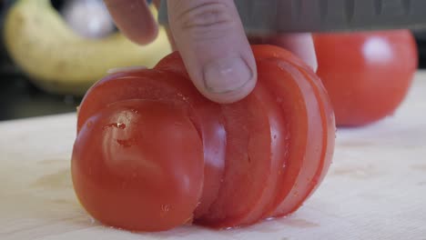 Cropped-close-up-of-men-at-home-slicing-tomatoe-on-cutting-board-using-sharp-knife