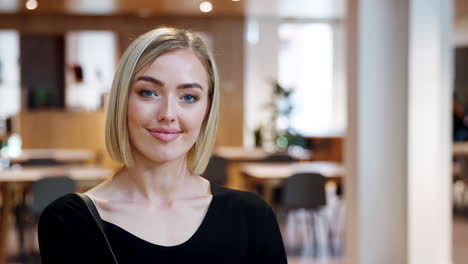 Young-white-woman-standing-in-a-business-lobby-looking-to-camera,-close-up