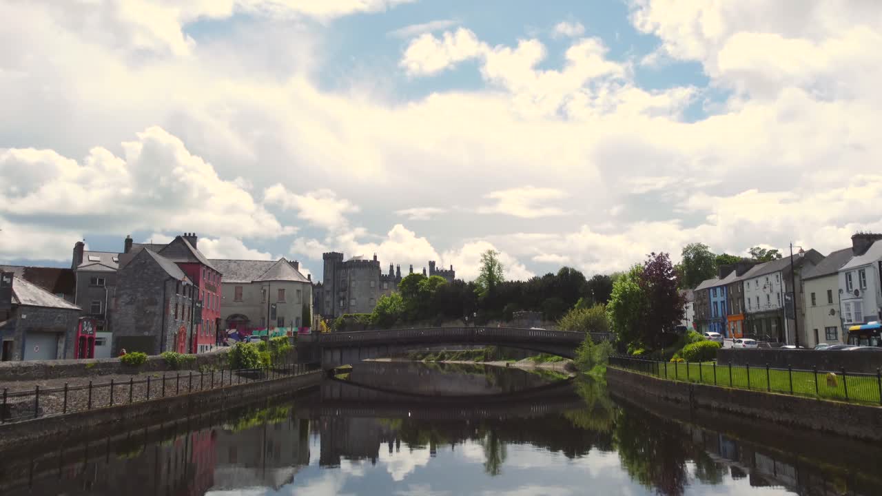 Aerial reveal footage along river of Kilkenny town with its castle and town centre.