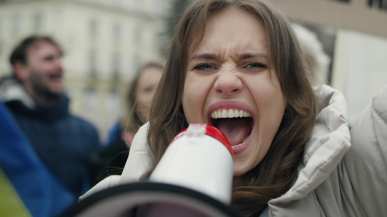 백인 여성이 카메라를 보고 젊은이들의 집회 앞에서 메가폰을 통해 비명을 지르고 있습니다.