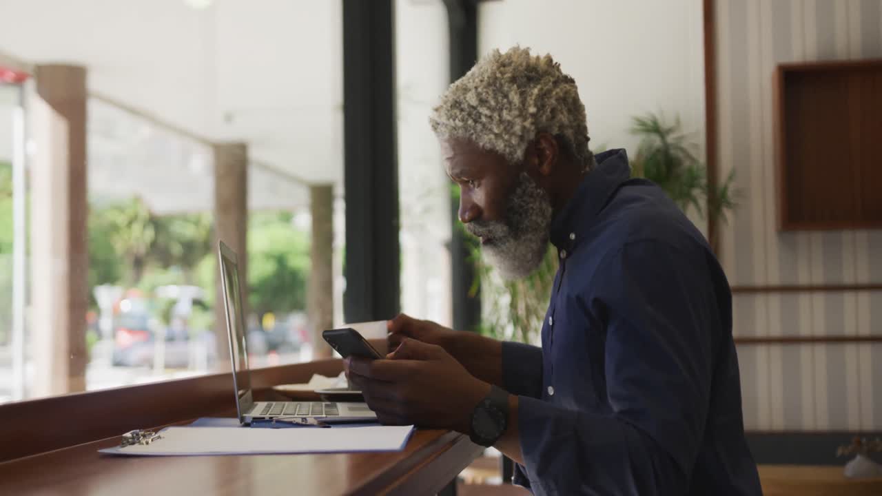 African american senior man using laptop and drinking coffee while sitting at cafe
