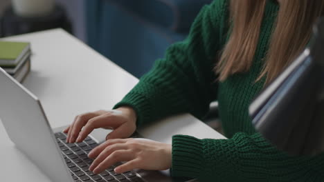 Una-Mujer-Joven-Y-Bonita-Está-Trabajando-Con-Una-Computadora-Portátil-En-La-Oficina-En-Casa-Escribiendo-En-El-Teclado-Y-Sentada-En-La-Mesa,-Detalles-De-Una-Foto-De-Una-Dama-Concentrada