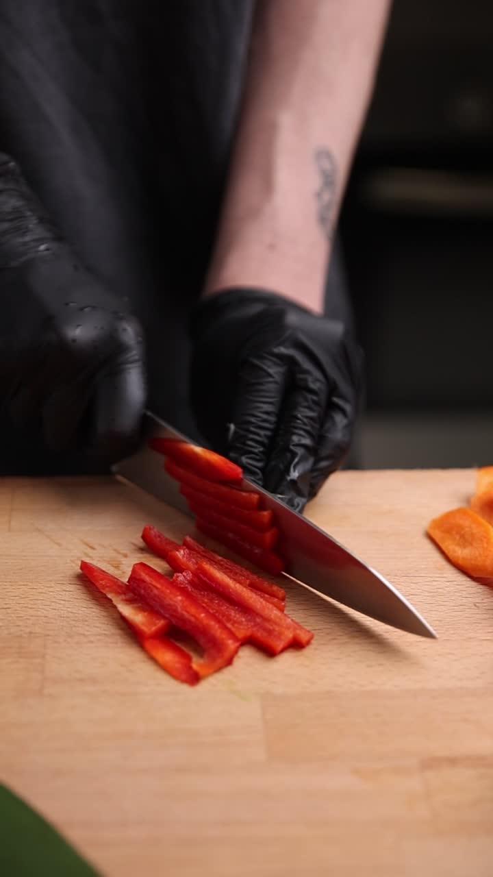 Mani dello chef con guanti neri che affettano peperone rosso su un tagliere