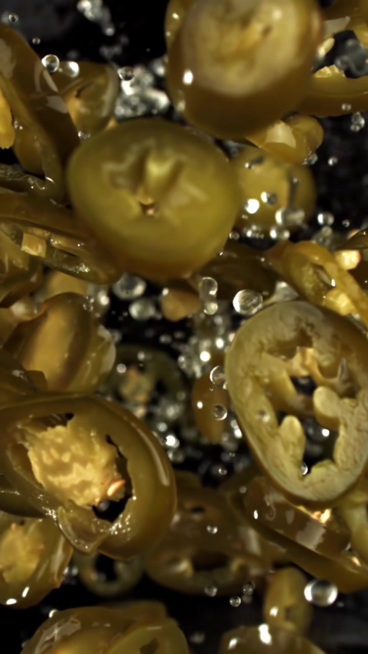 Fette di jalapeño sottaceto che cadono al rallentatore con gocce d'acqua