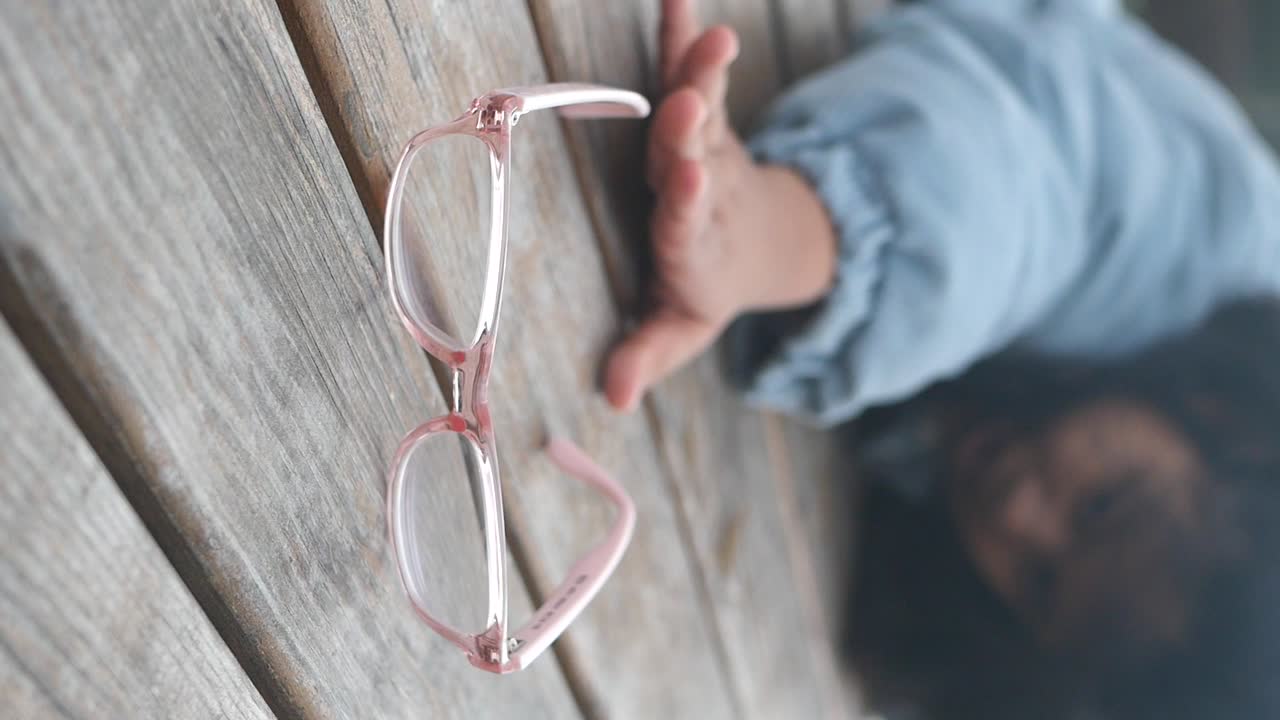 Pink glasses on a wooden bench with child's hands