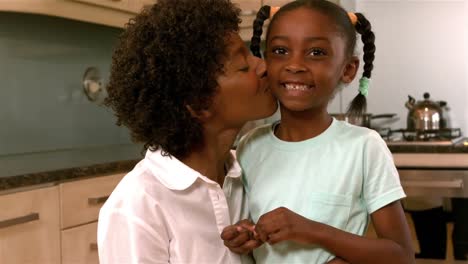 smiling mother kissing daughter in kitchen