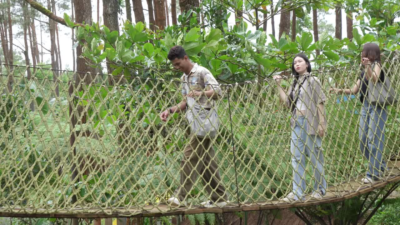 Young Asian Friends Crossing Rope Bridge in Forest Adventure