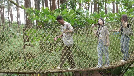 young asian friends crossing rope bridge in forest adventure