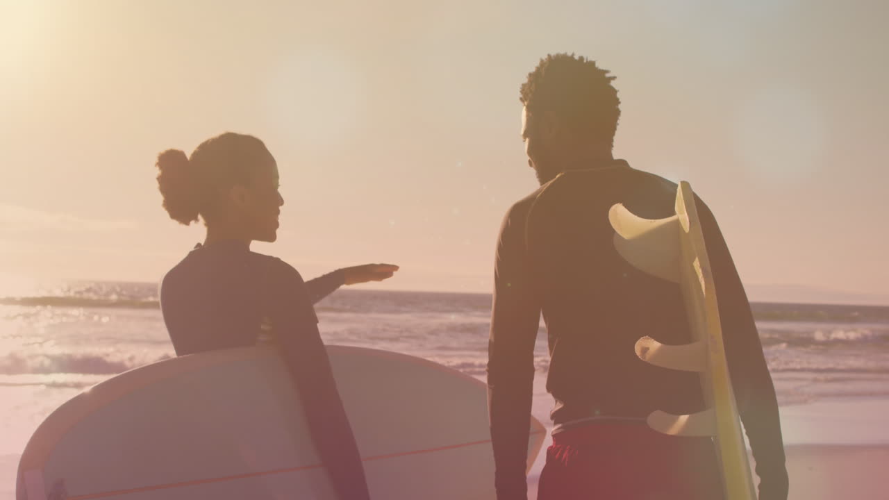 animación de puntos de luz sobre una pareja afroamericana con tablas de surf en la playa
