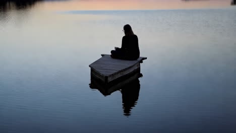woman sitting alone on a wooden dock at sunset