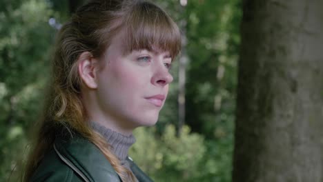 Beautiful-young-woman-looks-up-calmly-and-smiles-in-woods,-close-up