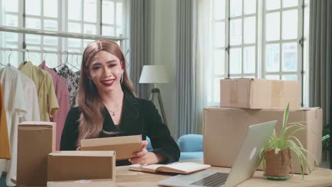 young asian transgender woman business owner with boxes on the table happy online sales job, get an order from customers, pose and smiles to camera