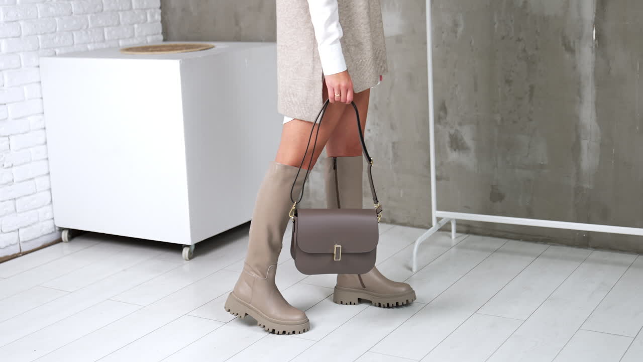 Girl in a stylish modern look showing grey boots and bag. Model turns to demonstrate her fashionable footwear and accessories. Studio backdrop.
