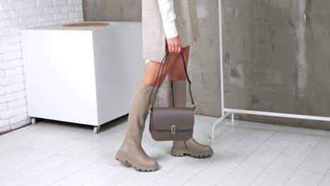 girl in a stylish modern look showing grey boots and bag. model turns to demonstrate her fashionable footwear and accessories. studio backdrop.