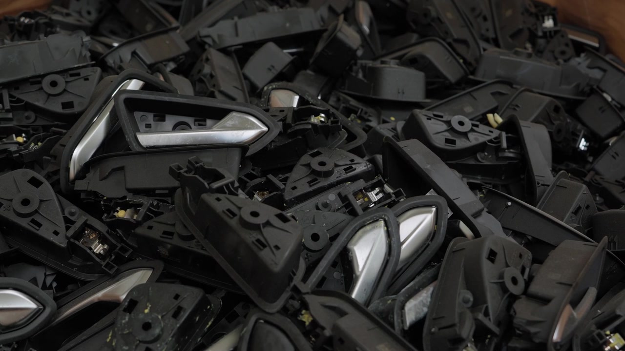 プラスチックリサイクルのために分類された、黒とクロムの自動車内装ドアハンドル部品の大量の山。