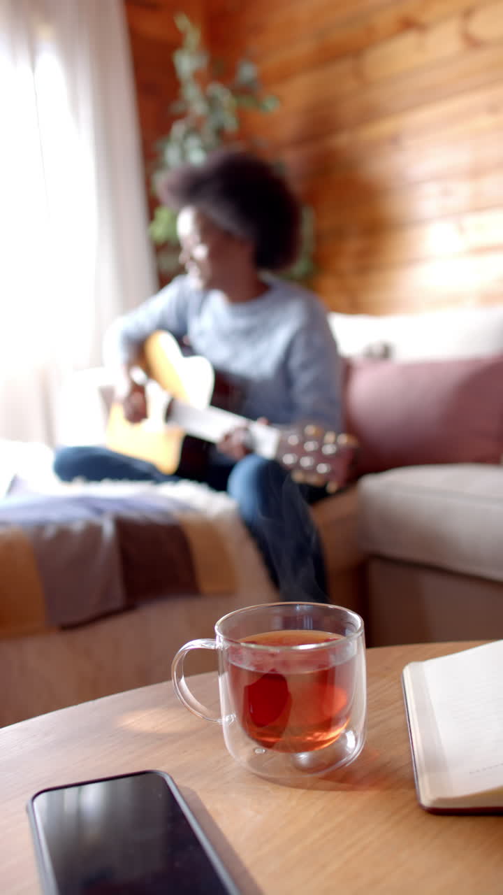 Video verticale di una felice donna afroamericana che suona la chitarra in soggiorno, al rallentatore.