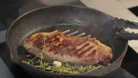 adding rosemary and garlic to frying steak