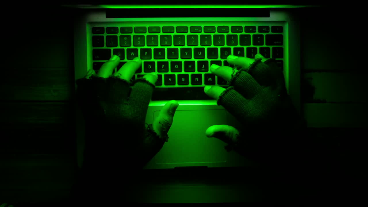 manos en guantes escribiendo en un teclado de portátil bajo luz verde