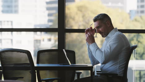 stressed or tired mature businessman working on laptop sitting at boardroom table