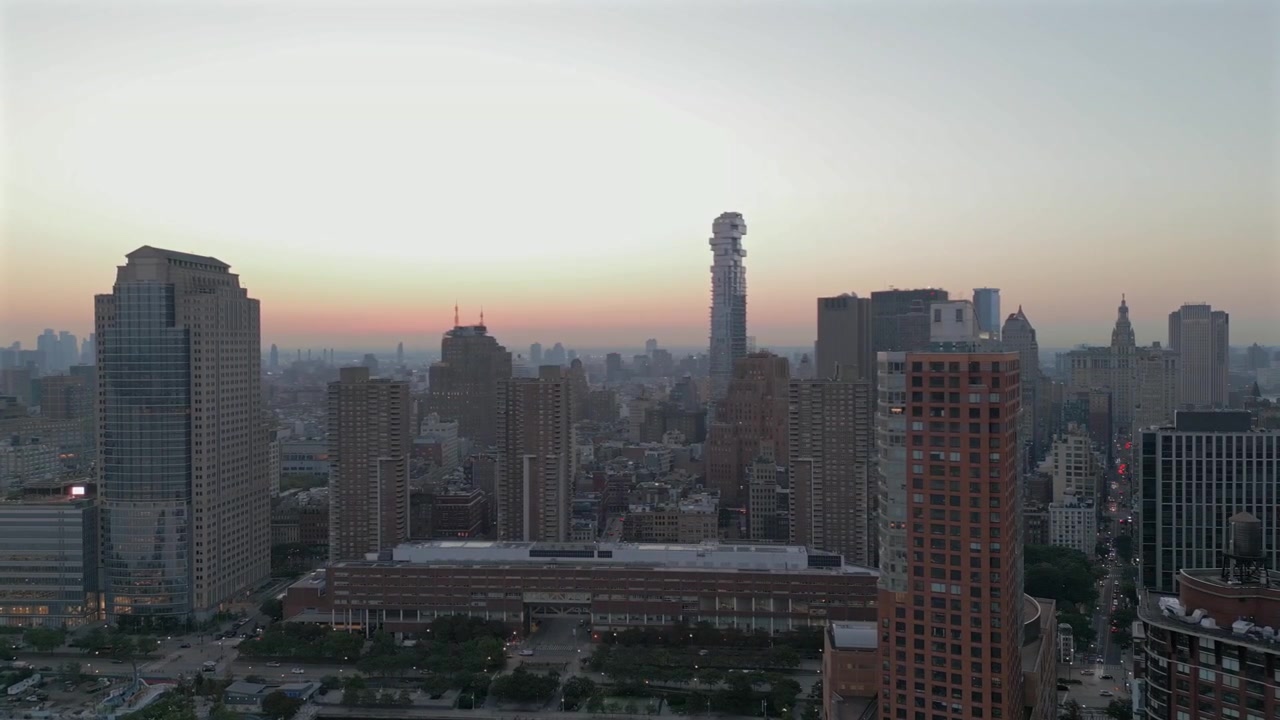 Filmagem aérea de drone em Tribeca, Nova Iorque, com movimento panorâmico e inclinação para o horizonte, mostrando a Jenga Tower e arranha-céus ao nascer do sol com céu dourado, e o porto em primeiro plano revelando o Rio Hudson.