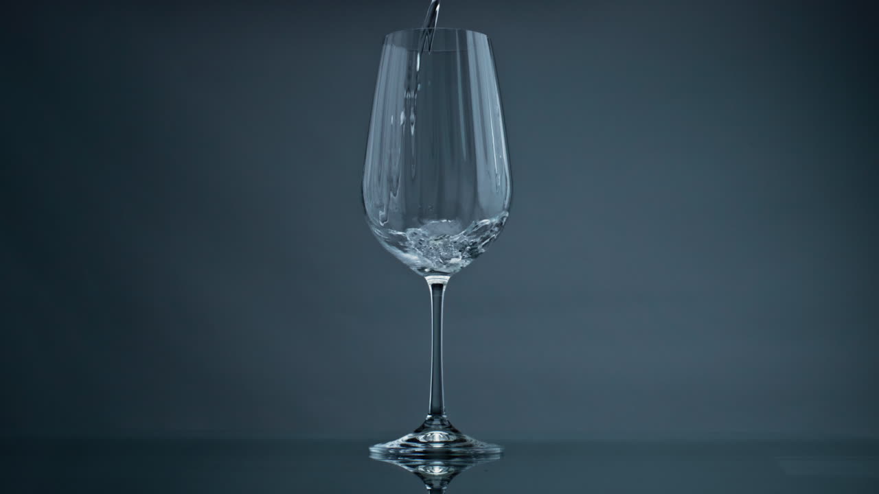 어두운 배경의 클로즈업에서 물을 부는 와인 글래스. 은 액체 스플래싱